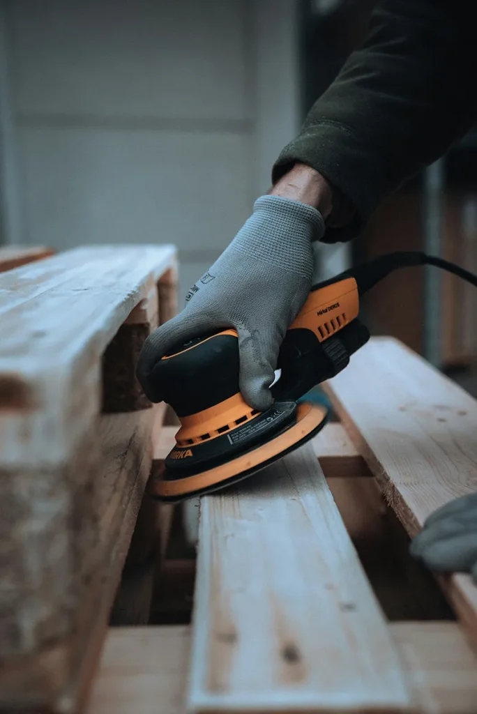Construction Laborer Using Orbit Sander on Block of Wood